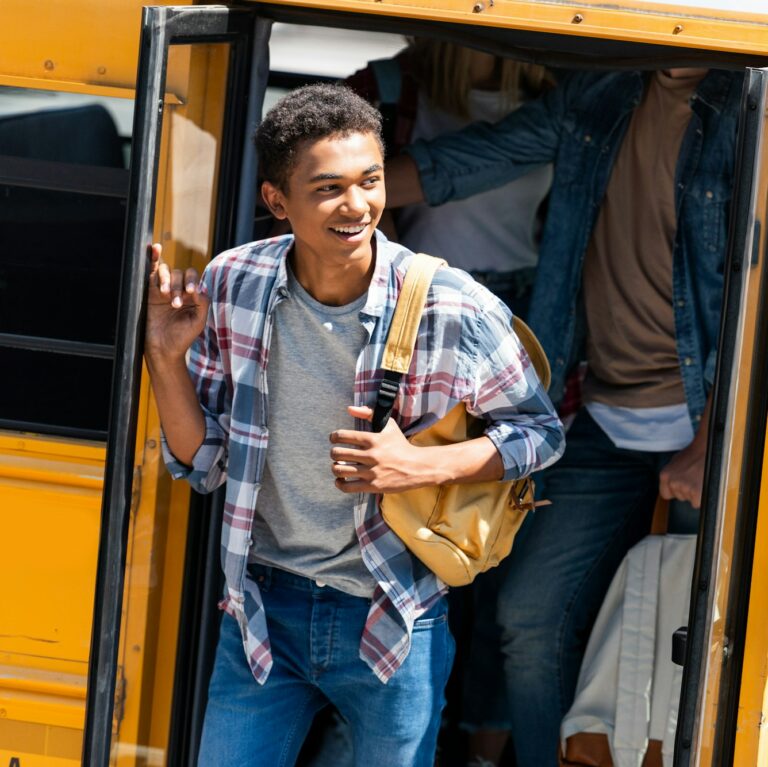 african american happy student walking out of school bus with classmates