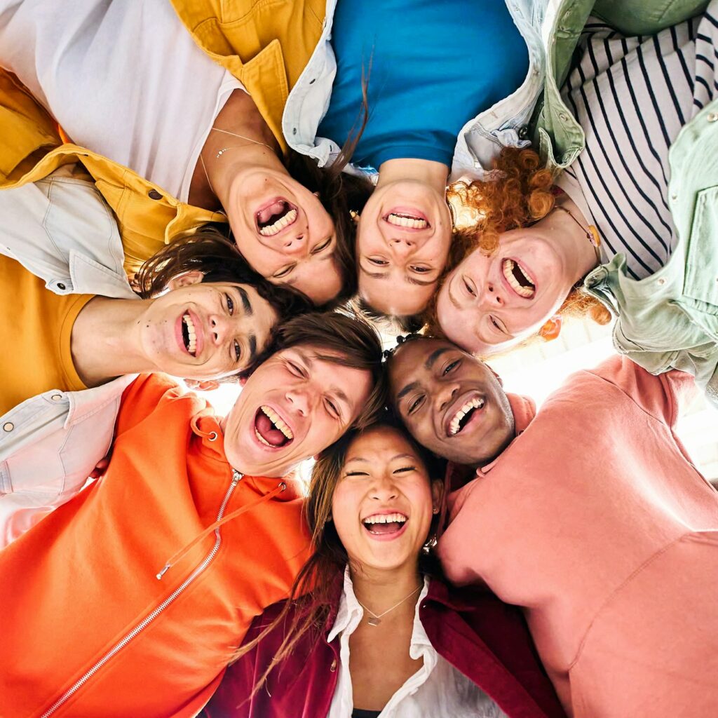 Vertical large multiracial group of smiling young people standing hugging looking at camera.